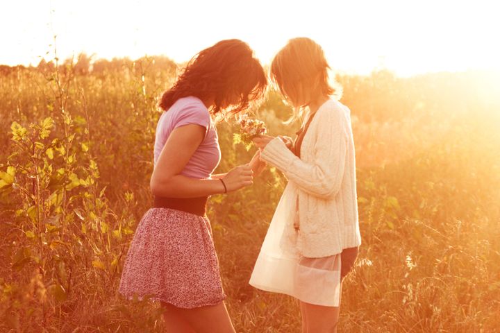 Girls holding flowers in field in sunlight, California.