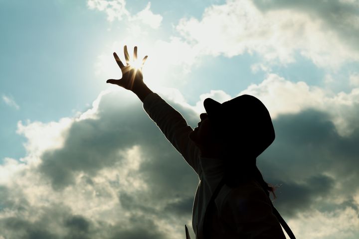 Young woman reaching hand towards sun