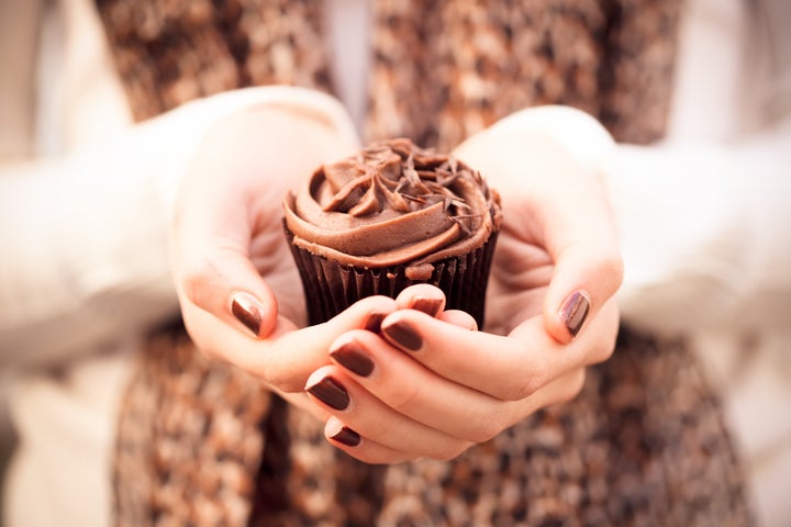 Girl holding chocolate cupcake in hands wearing leopard print scarf and brown nail polish.