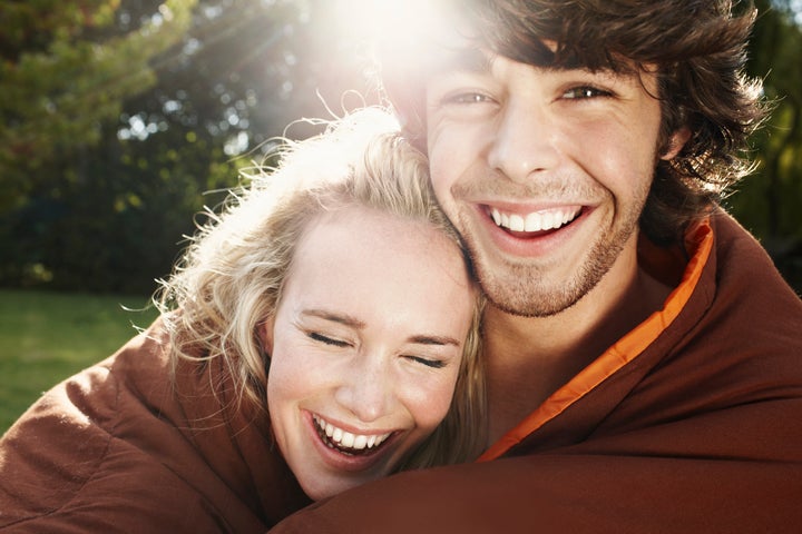 Young couple wrapped in sleeping bag, laughing