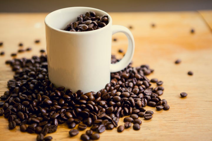 Fresh coffee beans around a white coffee mug and inside of it. Shot on a wood table surface. Coffee makes for an energetic start to every morning.