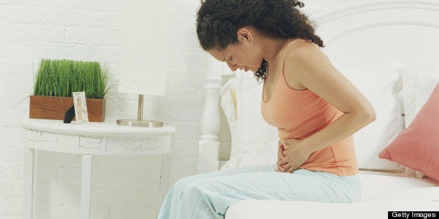 Woman sitting on bed holding stomach, head bowed