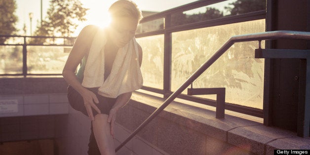 Woman stretching leg in metro station entrance at sunset.