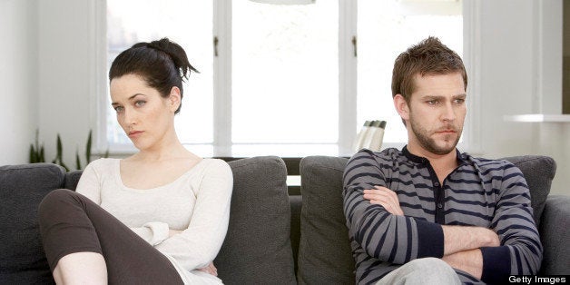 Couple sitting on sofa with arms folded, looking angry