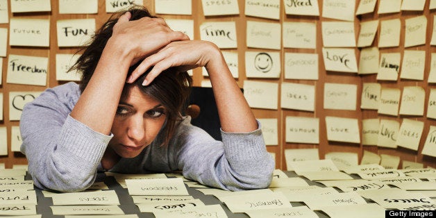 Woman at desk surrounded in adhesive notes, head in hands