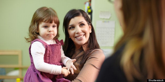 Caucasian female teacher and mom with baby girl talking in kindergarten. Horizontal shape, focus on background