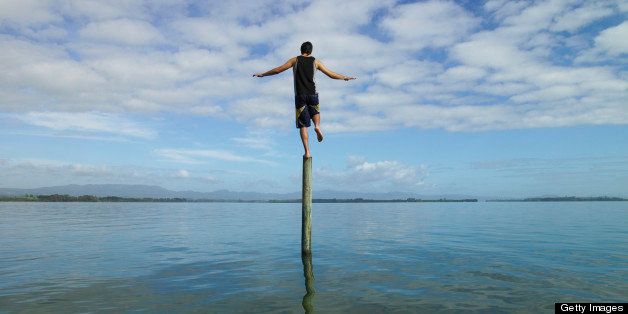 Young man balancing on a pole in the sea