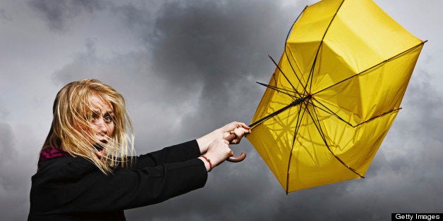 A pretty blonde woman looks horrified and helpless as her frayed and broken umbrella blows away from her, dragging her along, in a thunderstorm.
