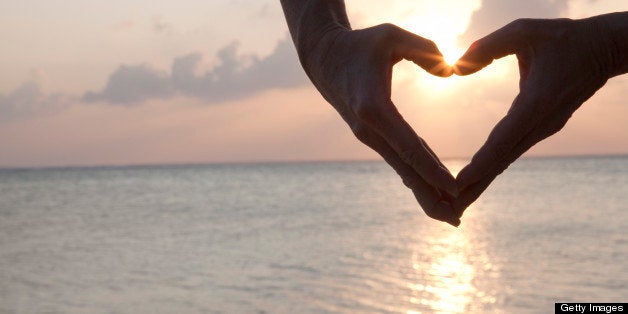 Detail of woman's hands making heart shape, sea