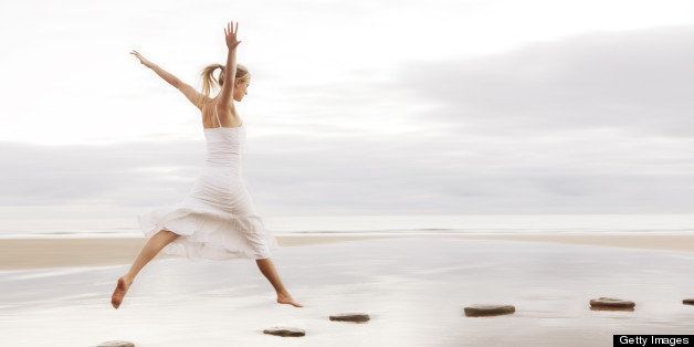 Woman in white dress jumping over stepping stones