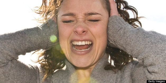 Outdoor portrait of Danish woman, 26 years old, screaming with arms on side of head and eyes closed