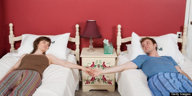 Young couple lying on single beds, holding hands