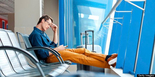 Young adult man waiting for his flight at the airport lounge and using a smart phone.