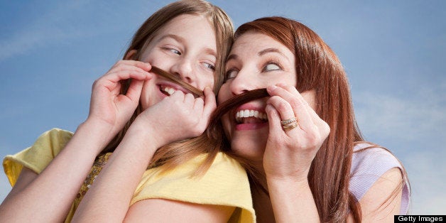 A mother and her daughter being silly together making mustaches out of their hair.