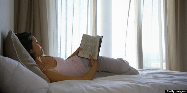 Woman reading book, lying on bed