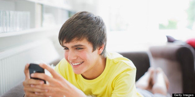 Smiling teenage boy in living room text messaging on cell phone