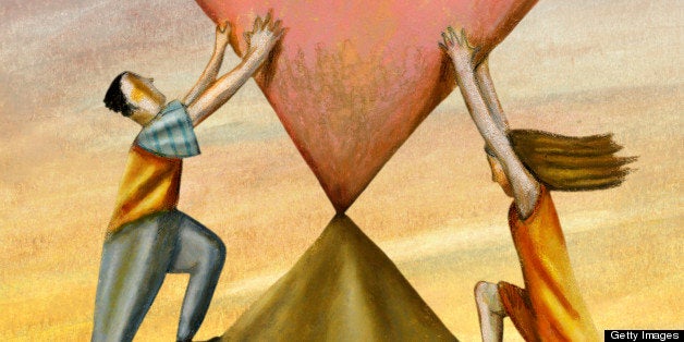 A man and woman holding a heart on top of a mountain peak