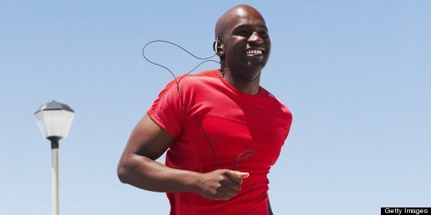 black male with headphones running on beach promenade by coloured beach huts wearing a red t shirt