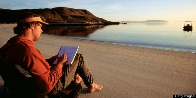 Man sitting on beach writing in journal.