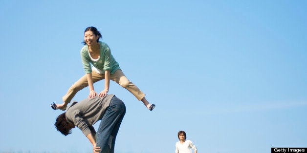 Three people playing leapfrog on grass