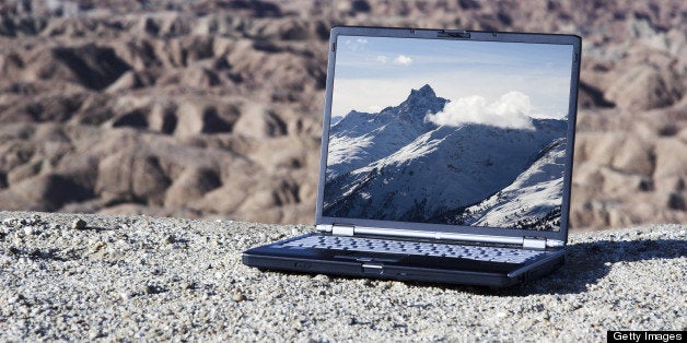 Global warming concept. A modern laptop computer sits in a desert landscape with snow covered mountains on the screen. All logos have been removed.