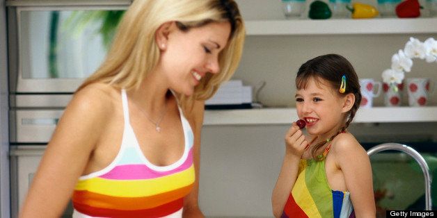 Mother Preparing Food in Kitchen and Daughter Looking at Her While Eating a Cherry