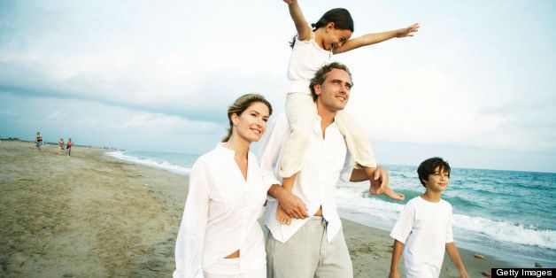 Family on beach, girl (6-8) on father's shoulders, arms outstretched