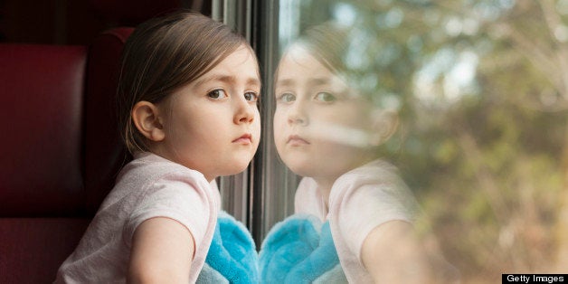 Young girl staring out of a window, with her mirror image reflecting back at her.