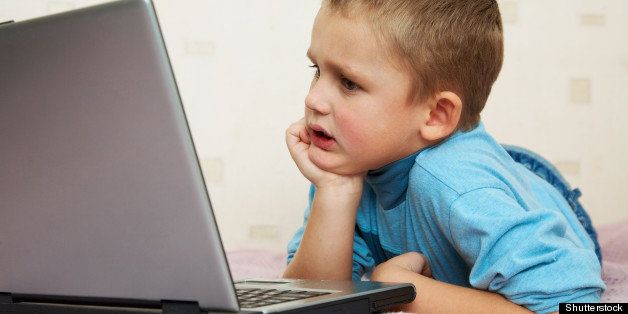 School-age boy sitting in front of the monitor laptop at home on the couch.