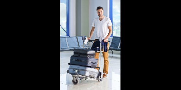 Full lenght portrait of a mid adult man pushing a luggage trolley with suitcases at the airport and smiling at the camera.