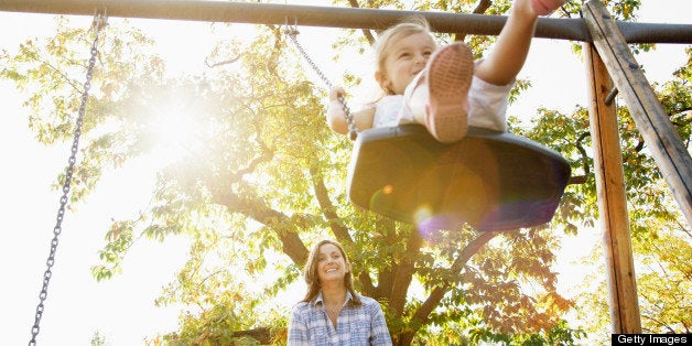 Mother pushing daughter on swing in sunny park