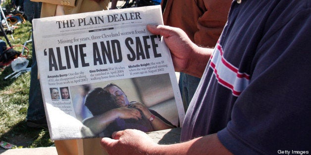 CLEVELAND, OH - MAY 7: A man shows page one of The Plain Dealer newspaper to a friend while people gather along Seymour Avenue near the house where three women, who disappeared as teens about a decade ago, were found alive, May 7, 2013 in Cleveland, Ohio. Amanda Berry, who went missing in 2003, Gina DeJesus, who went missing in 2004, and Michelle Knight, who went missing in 2002, managed to escape their captors on May 6, 2013. Three suspects, all brothers, were taken into custody. (Photo by Bill Pugliano/Getty Images)