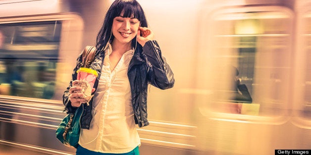 New Yorker girl enjoying in the subway with music and coffee against a train.