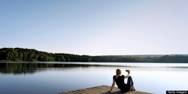 Woman taking pictures on pier over a pond surrounded by woods.