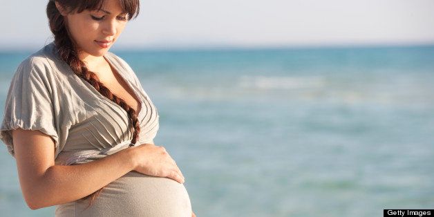 Pregnant woman holding her stomach on beach