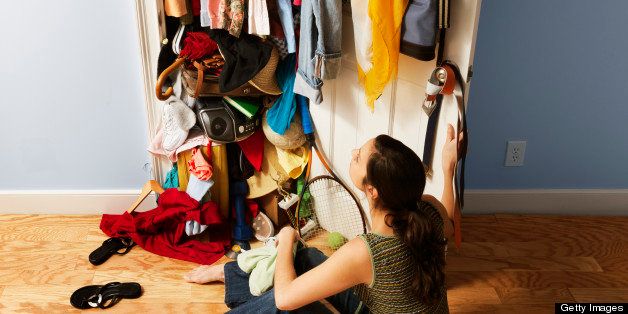 Young woman sitting on a hardwood floor gazing at her unorganized closet. Vertical shot.