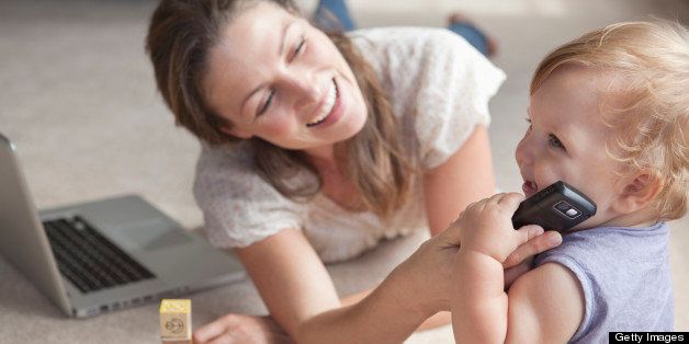 Smiling woman working on laptop while baby playing with mobile phone