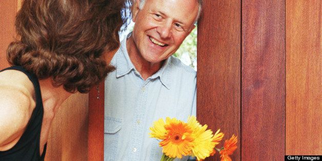 Mature woman opening door for man holding flowers, smiling
