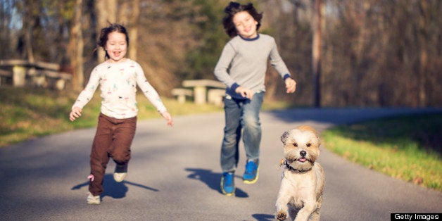 A young boy and girl enjoy chasing their pet dog down the road