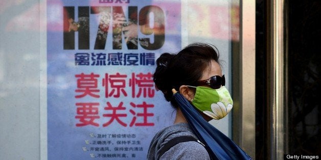 A woman wears a face mask as she walks past a poster showing how to avoid the H7N9 avian influenza virus, by a road in Beijin