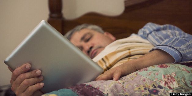 Middle aged man reading in bed on his tablet.