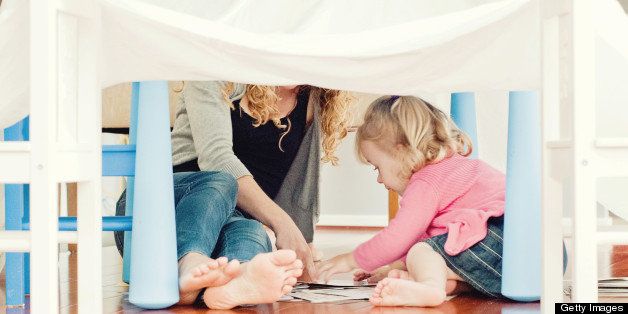 Girl with blonde hair playing with her mother under cubbyhouse.