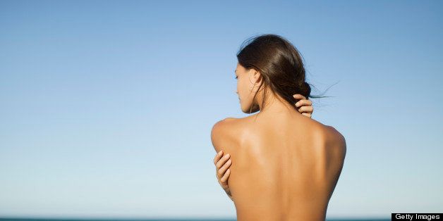 Naked woman looking at ocean, rear view