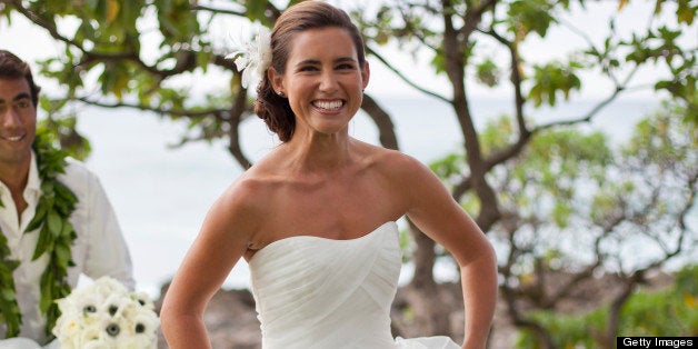 A groom helps his wife by carrying her train and her bouquet as they come back from the beach