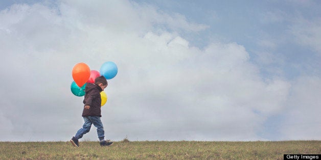 A young boy carrying his colourful birthday balloons through a field in North Yorkshire, England. Negative Space