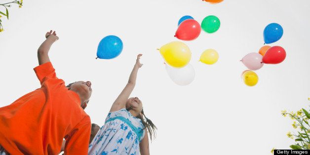 Boy and girl (6-9 years) releasing balloons in sky