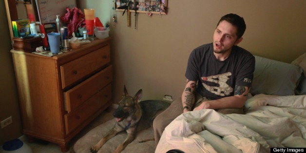 HANOVER PARK, IL - APRIL 27: Army veteran Brad Schwarz sits in his bedroom with his service dog Panzer at his side April 27, 2012 in Hanover Park, Illinois. Schwarz, who suffers from post traumatic stress disorder (PTSD), uses a service dog to help him cope with issues related to the disorder which he has dealt with since returning from a 2008 tour in Iraq. Panzer, who sleeps next to Schwarz's bed, is trained to wake him when he has nightmares. In addition to suffering from PTSD Schwarz has memory loss related to Traumatic Brain Injury (TBI) and he must walk with a cane because of vertebrae and nerve damage in his back and legs. Ten days before he was scheduled to rotate home from a 15-month deployment in Iraq, his second, the Humvee in which he was riding was struck by an Improvised Explosive Device (IED). Of the 5 soldiers riding in the vehicle, which caught fire after the explosion, Schwarz was the only one to survive. (Photo by Scott Olson/Getty Images)