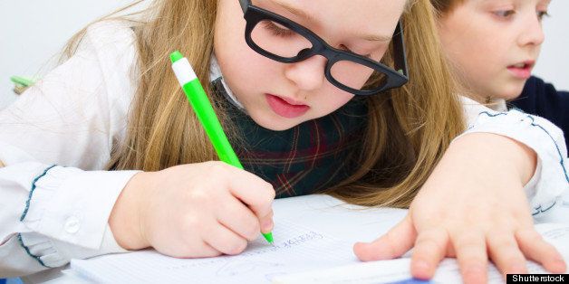 Little schoolchildren writing at school in workbook