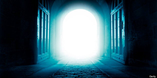 A cobbled street leads to the open gates of a castle, a welcoming light hides what may lay beyond.