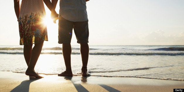 Couple holding hands near waves on tropical beach at sunrise